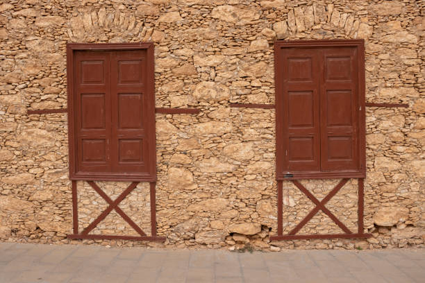 Natural stones mainly of a brown color, creating a wall of a house. Two old style windows with closed shutters. Tiscamanita, Fuerteventura, Canary Islands, Spain.