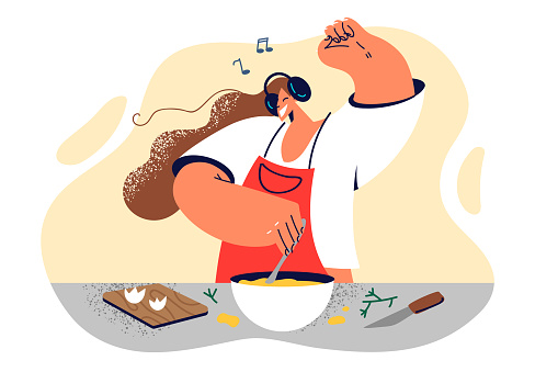 Woman housewife cook breakfast dancing listening to incendiary music enjoying weekend morning. Girl in headphones learns to cook by shaking eggs in large bowl to feed family delicious lunch