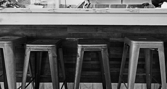 Four stools at a tall counter at a restaurant.   Black and white.