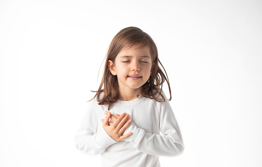 Little girl is holding her hands over her heart, white background.