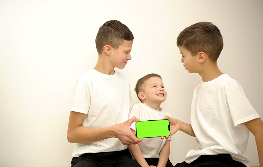 family photo three siblings are talking on a white background holding a green screen chroma key phone they are smiling and telling something