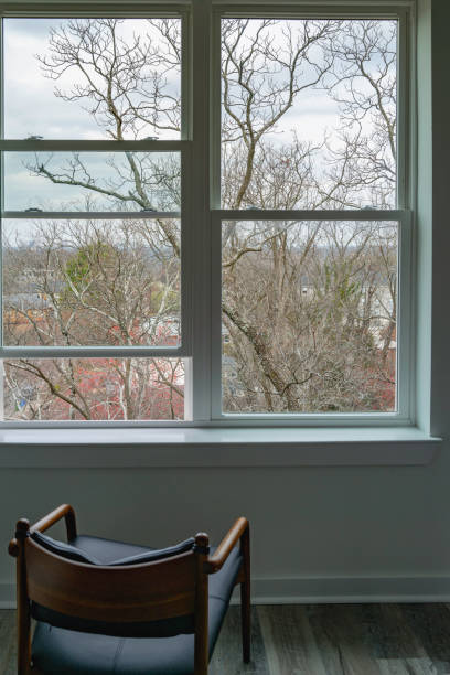 istock Interior window view of red spring sprouts of barren maple tree branches, empty chair, and abstract geometry of the white frames, city home landscape 1469249135