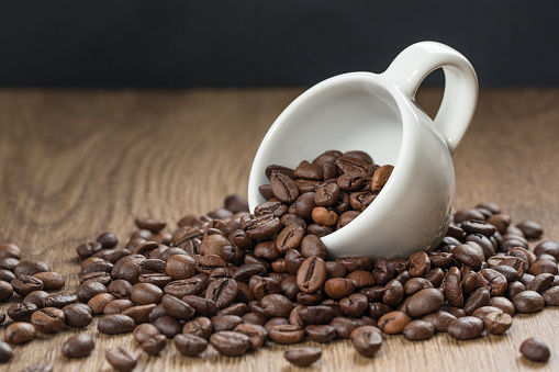White cup with roasted coffee beans close up, on wooden background. Good mood