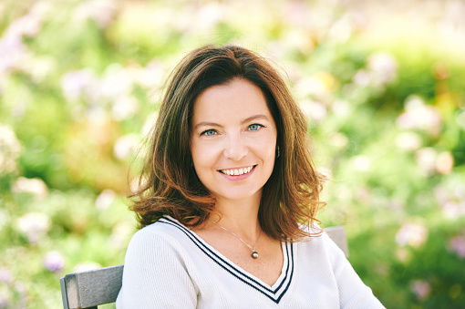 Outdoor portrait of beautiful 40 - 45 years old woman sitting on bench ib green park, healthy lifestyle