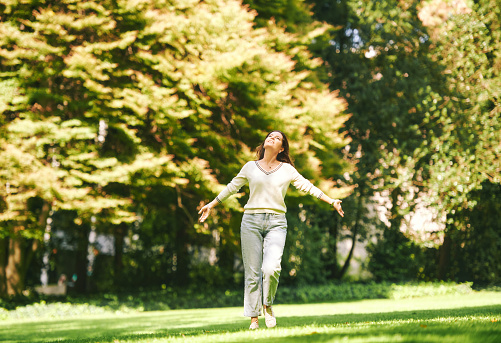 Outdoor portrait of happy and healthy 40 - 45 year old woman enjoying nice sunny day in park, arms wide open