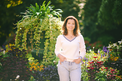 Outdoor portrait of happy beautiful 40  - 45 year old woman, wearing white pullover, posing in park on a very sunny day, healthy lifestyle