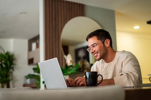 Latino ethnic man between the ages of 25-35 is using his laptop to surf the internet at home