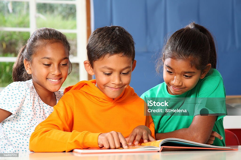 Three primary school children in class reading and learning together Cheerful young primary school children reading and learning together in the classroom - Canon 5D MKII Book Stock Photo