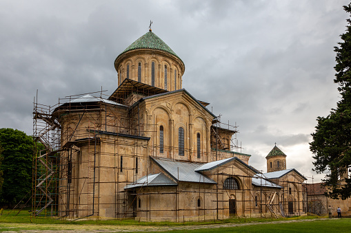 Gelati Monastery, medieval monastic complex near Kutaisi, Georgia founded by King David IV, view with scaffolding during restoration process, dark cloudy sky.