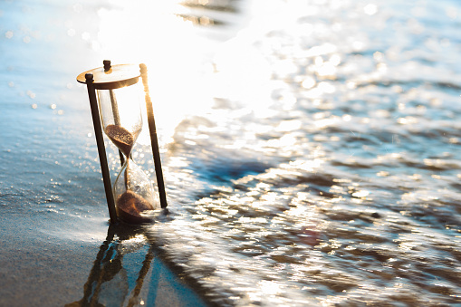 Vintage sandglass lost on the beach. Rustic watch buried in sand.