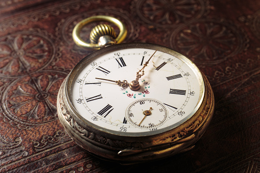 one gray old pocket watch with an open mechanism lies on a black wooden table