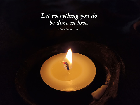 Bible verse quote - Let everything you do be done in love. Corinthians 16:14 on a candle light shine in the dark. Black background. Christianity concept.
