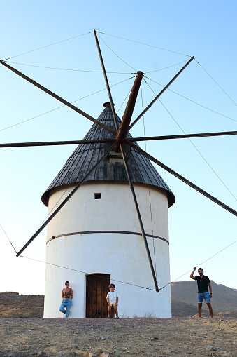 Parents and their little kid posing in front of a windmill in el Pozo de los Frailes Village, in Cabo de Gata National Park, Nijar, Andalucia, Spain.