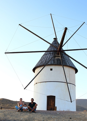 Parents and their little kid posing in front of a windmill in el Pozo de los Frailes Village, in Cabo de Gata National Park, Nijar, Andalucia, Spain.