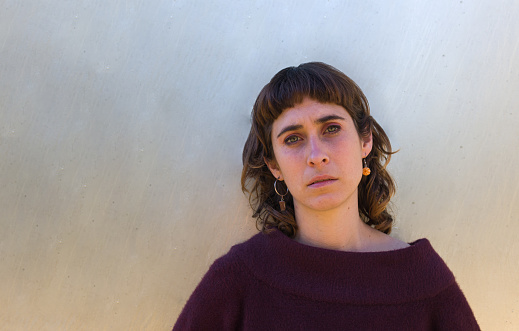 hipster woman looking at camera with a concerned expression ahead a plain background | headshot | green eyes