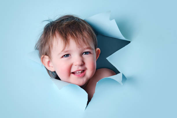 istock Happy baby in a hole on a paper blue background. Torn child head studio background, copy space. Kid aged one year six months 1469315909