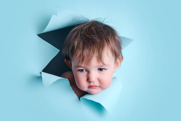 Sad baby in a hole on a paper blue background. Torn child's head studio background, copy space. Kid aged one year six months