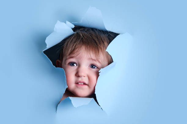 istock Sad baby in a hole on a paper blue background. Torn child's head studio background, copy space. Kid aged one year six months 1469316196