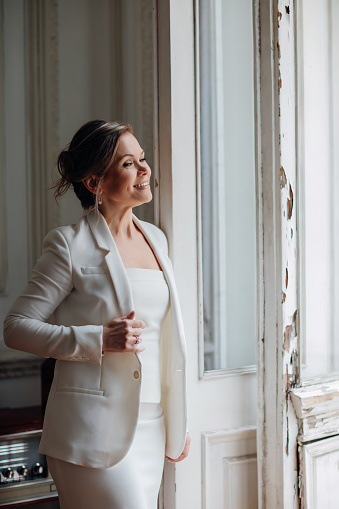 a beautiful and confident woman in a white suitat the old window. the concept of office clothing for a business woman. femininity in business style. image of the bride.