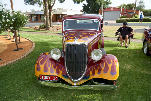 a Red hot rod with yellow flames mural at Tongala show and shine Victoria Australia, with the owner resting in a chair in the shade