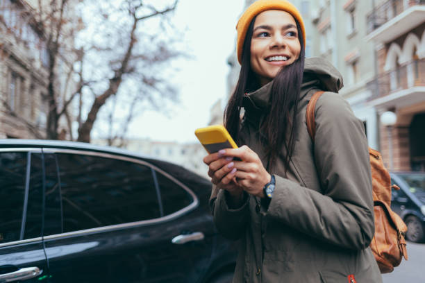 woman with winter jacket and hat uses mobile phone - coat warm clothing one person joy imagens e fotografias de stock