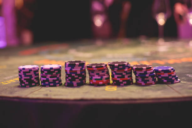 Casino concept, casino table with roulette in motion, with casino chips, tokens, the hand of croupier, dollar bill money and a group of gambling rich wealthy people playing bet in the background stock photo
