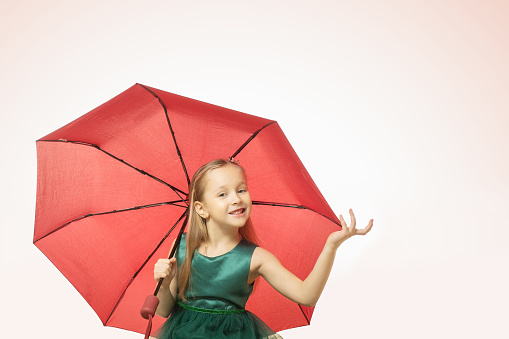 Portrait of a pretty little girl with red ambrella on pink background.