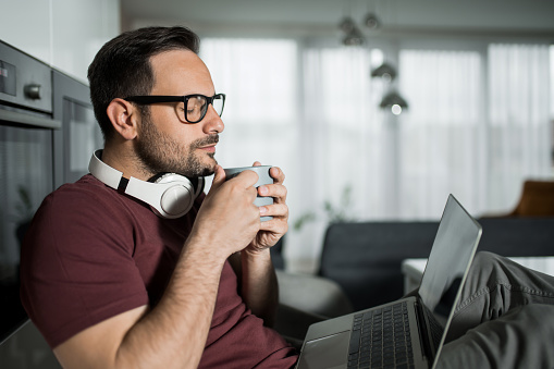 Tranquil man working on laptop and enjoying his morning coffee at home.