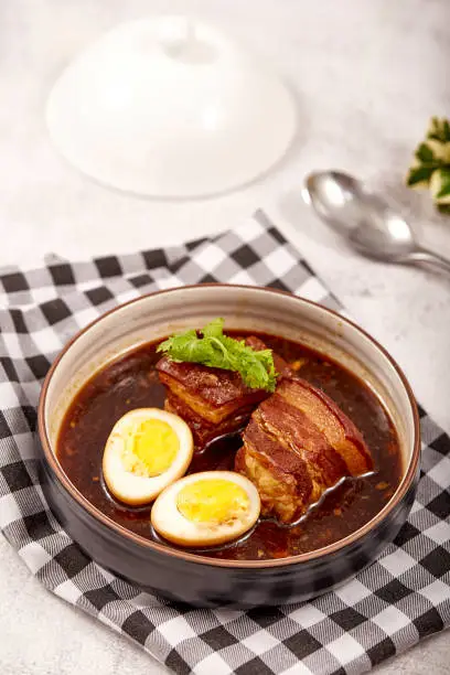 Photo of Egg and Pork in Sweet Brown Sauce in bowl  placed on tablecloth, 2 boiled eggs, braised pork and cilantro. popular food in asia.