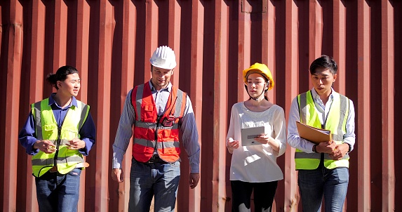 Group of engineer workers team wearing safety hard helmet talking and walking at logistic cargo container yard background