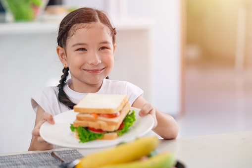 Asian cute daughter happy enjoy eating healthy food morning meal vegetable salad sandwich