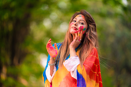 Happy young beautiful girl playing with colours on the occasion of Holi festival at an outdoor park. Holi also known as festival of colours , a popular Indian festival celebrated across India and Nepal.