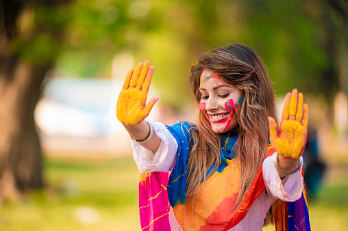 Portrait of happy Indian woman with colourful hands celebrating Holi with powder colours. Concept of Indian festival Holi celebration in park.