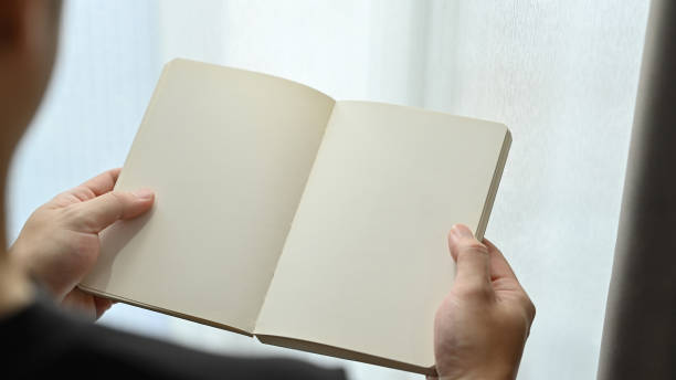 istock Over shoulder view of hands holding a blank opened notebook. Copy space for your advertise text. 1469398018