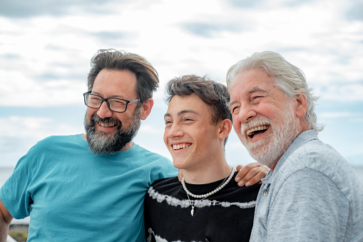 Portrait of three males laughing, grandfather, son and grandson stay together at the beach, smiling group of multi generation family enjoying good company expressing love and happiness