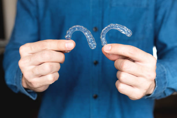 istock Caucasian young man shows invisible aligner for teeth correction. A man's hand holds plastic braces for dentistry to straighten his teeth, against the background of a blurred self 1469401306