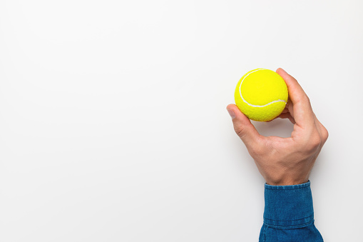 Man's hand holding a tennis ball on a white background, space for advertising.
