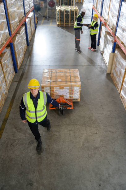 worker in auto parts warehouse use a handcart to work to bring the box of auto parts into the storage shelf of the warehouse waiting for delivery to the car assembly line - automobile industry transportation indoors vertical imagens e fotografias de stock