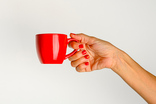 hands of a young woman holding a red cup of coffee, white background