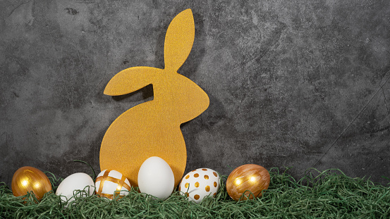 Happy Easter background banner holiday greeting card - Golden Easter bunny and easter eggs on green grass and concrete wall