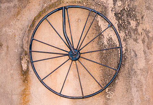 Old rod iron bicycle wheel with spokes on dirty concrete stained wall