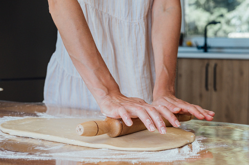 Close up of young woman rolling dough with rolling pin for homemade bakery.