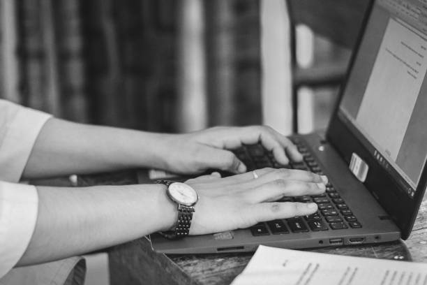 Grayscale of a human hand typing on a laptop