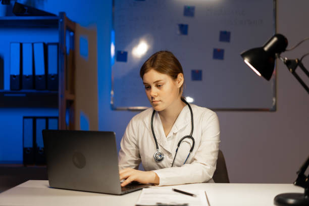 istock Attractive doctor in white coat sitting at table using laptop during night shift. 1469449438