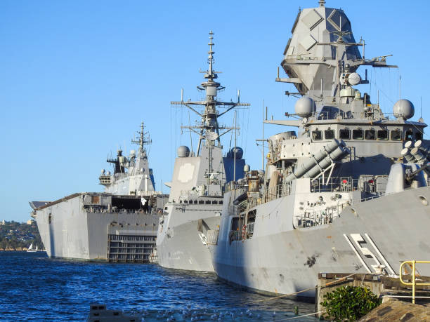 Sydney Navy Week Ships The frigate HMAS Arunta (right), destroyer HMAS Sydney (centre) and amphibious assault ship HMAS Canberra (left) of the Royal Australian Navy.  They are docked at Garden Island, Sydney Harbour, in preparation for an open day to the public during Navy Week, the first open day since the Covid pandemic.  A shadow from a skyscraper in the central business district is starting to make a shadow on the hull of HMAS Canberra.   This image was taken at sunset from Woolloomooloo Bay on 25 February 2023. australian navy stock pictures, royalty-free photos & images