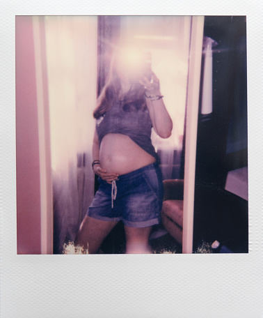 Pregnant woman makes selfie using Instant camera and a mirror.  Polaroid photo.