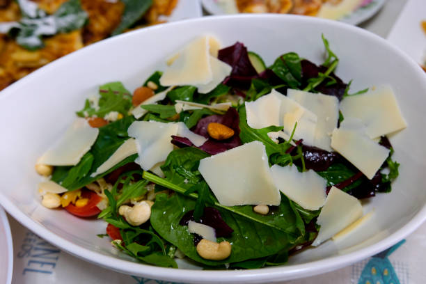 istock salad with parmesan cheese different vegetables nuts leaves arugula tomatoes bell peppers hazelnuts almonds cilantro spinach on a white plate close-up 1469457217
