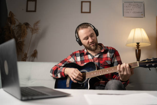 istock Focused man learning online playing guitar using laptop at home. 1469457234