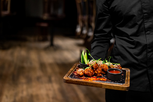 Waiter hold plate with chicken wings in restaurant or pub