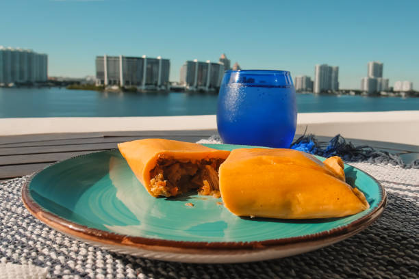 Opened Hallaca or Tamale over a rustic table and a blue dish with a drink, Mexican and Venezuelan traditional food with a Miami, Florida cityscape blurred background
